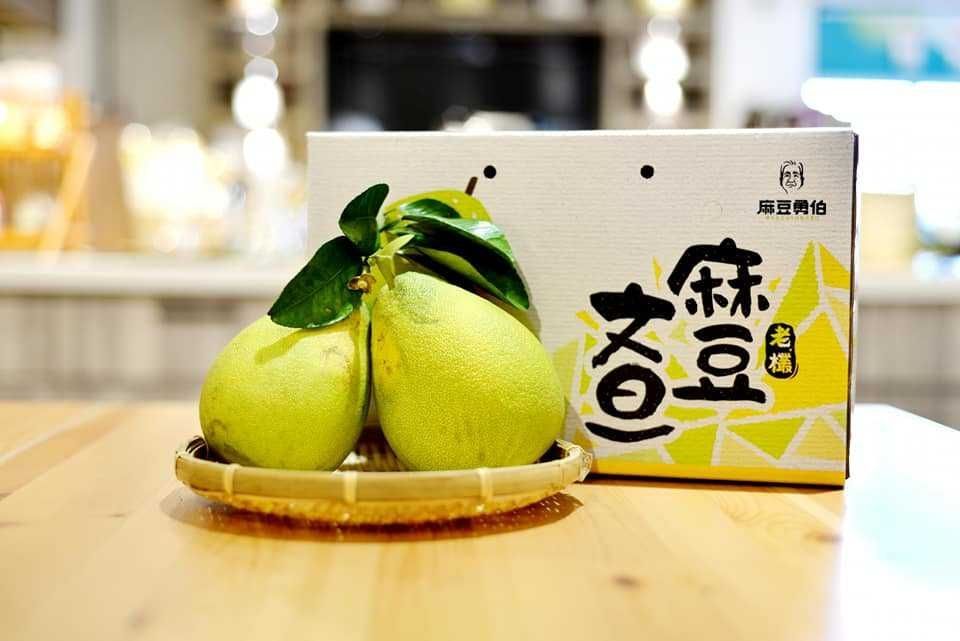 一箱柚子放在一張木桌上，旁邊還有一籃柚子。