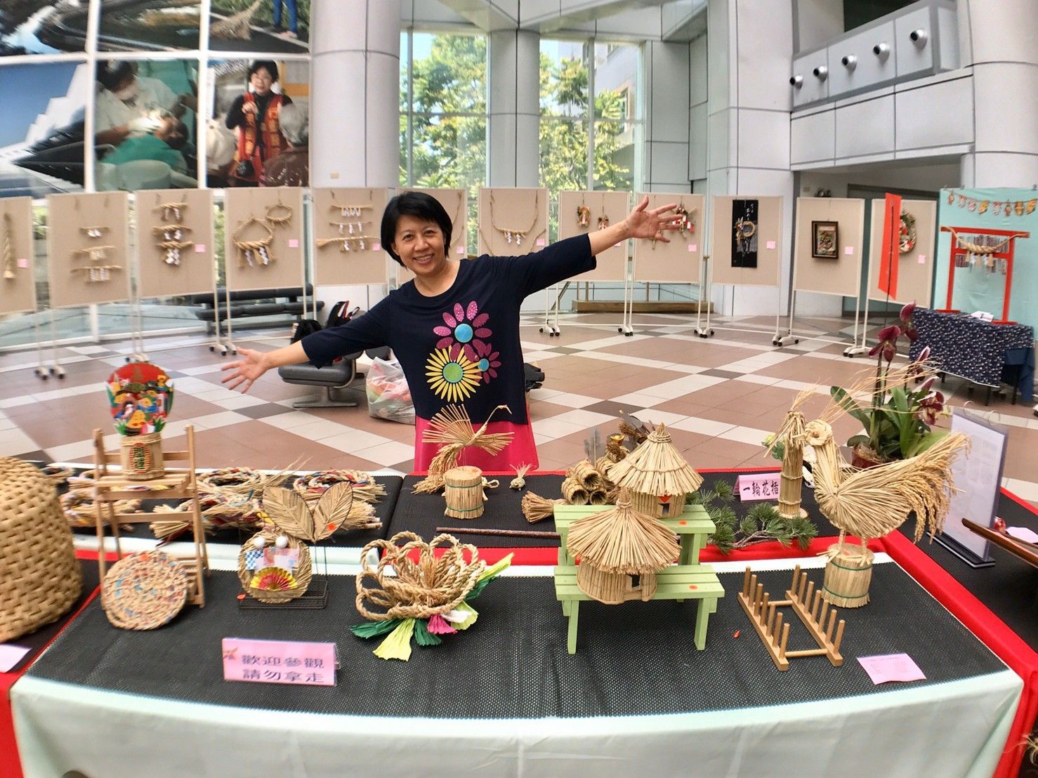 一位婦女站在一張桌子前，桌子上擺滿了各種工藝品。