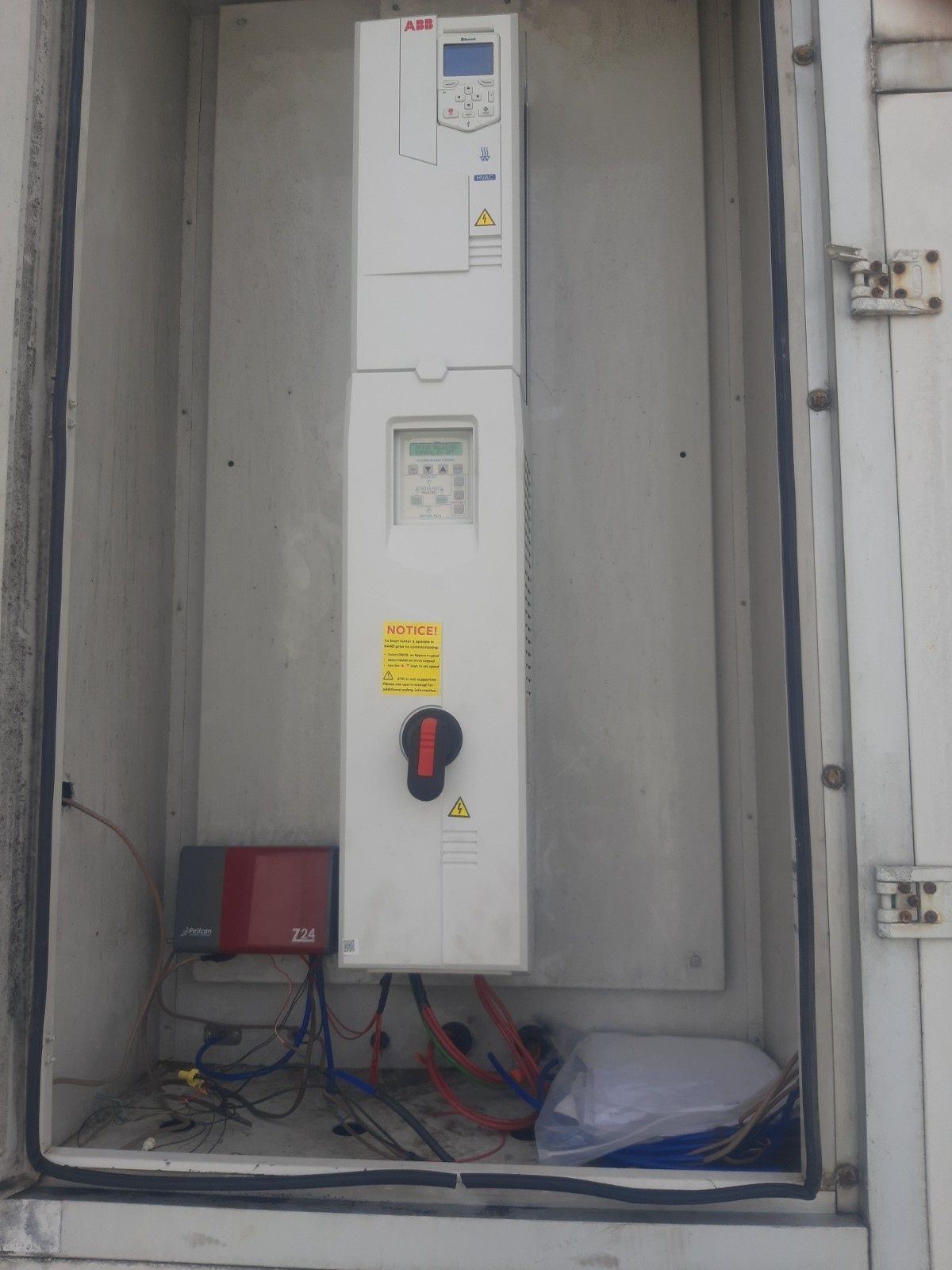An ABB variable frequency drive (VFD) mounted inside a metal enclosure, with a small red data module and wiring below.