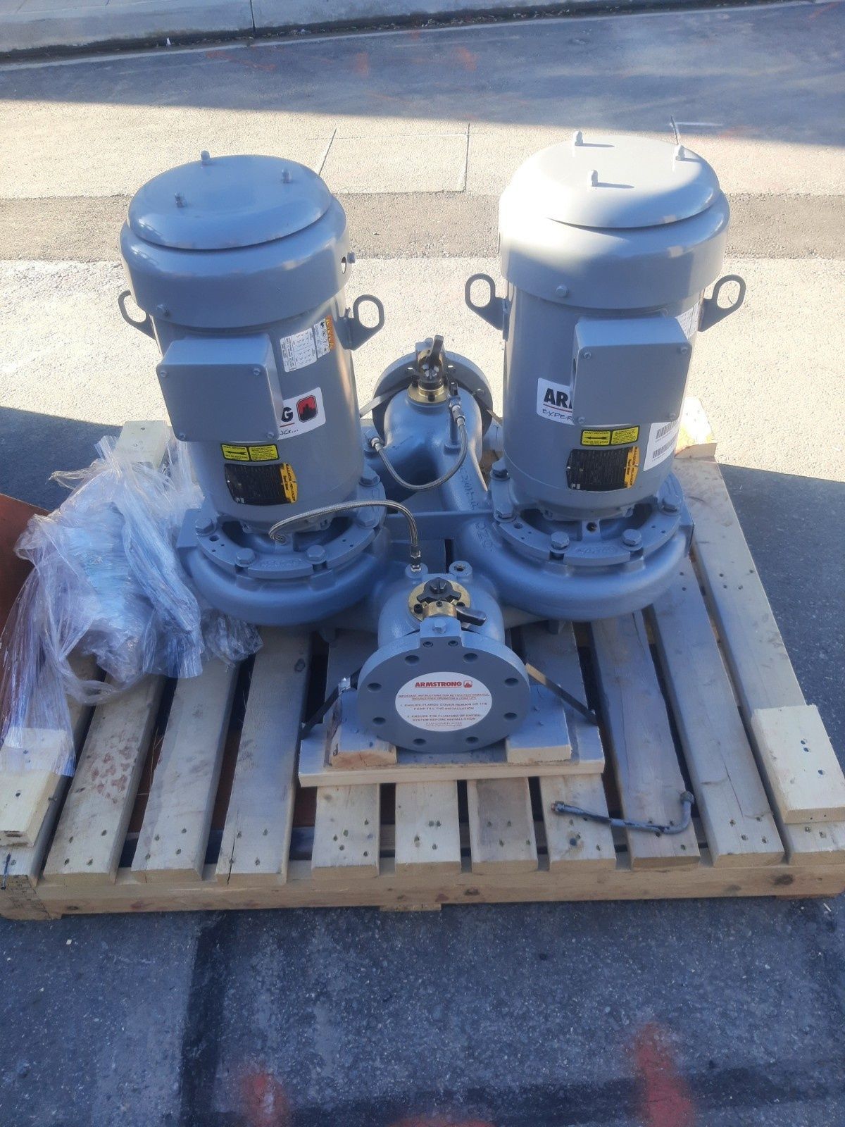 Two grey vertical pumps mounted on a wooden pallet outdoors.