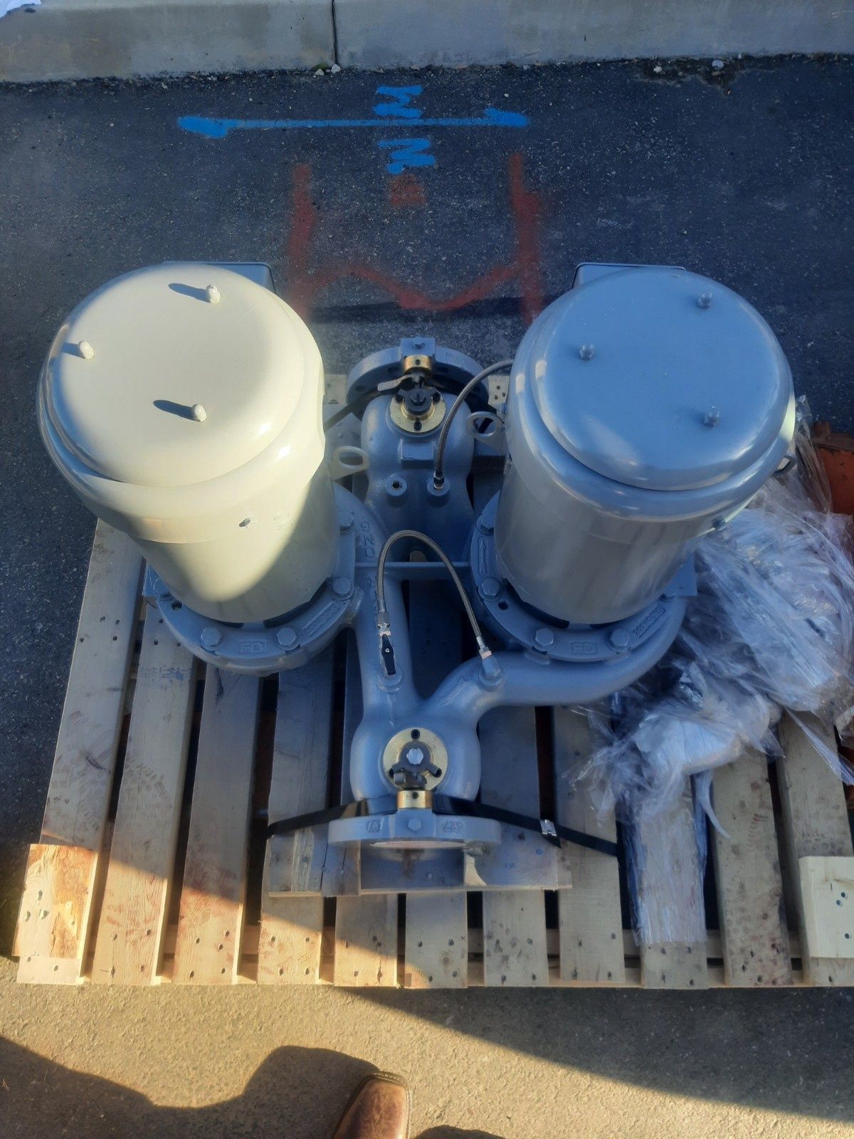 A dual industrial pump assembly with gray motors mounted on a wooden shipping pallet outdoors.
