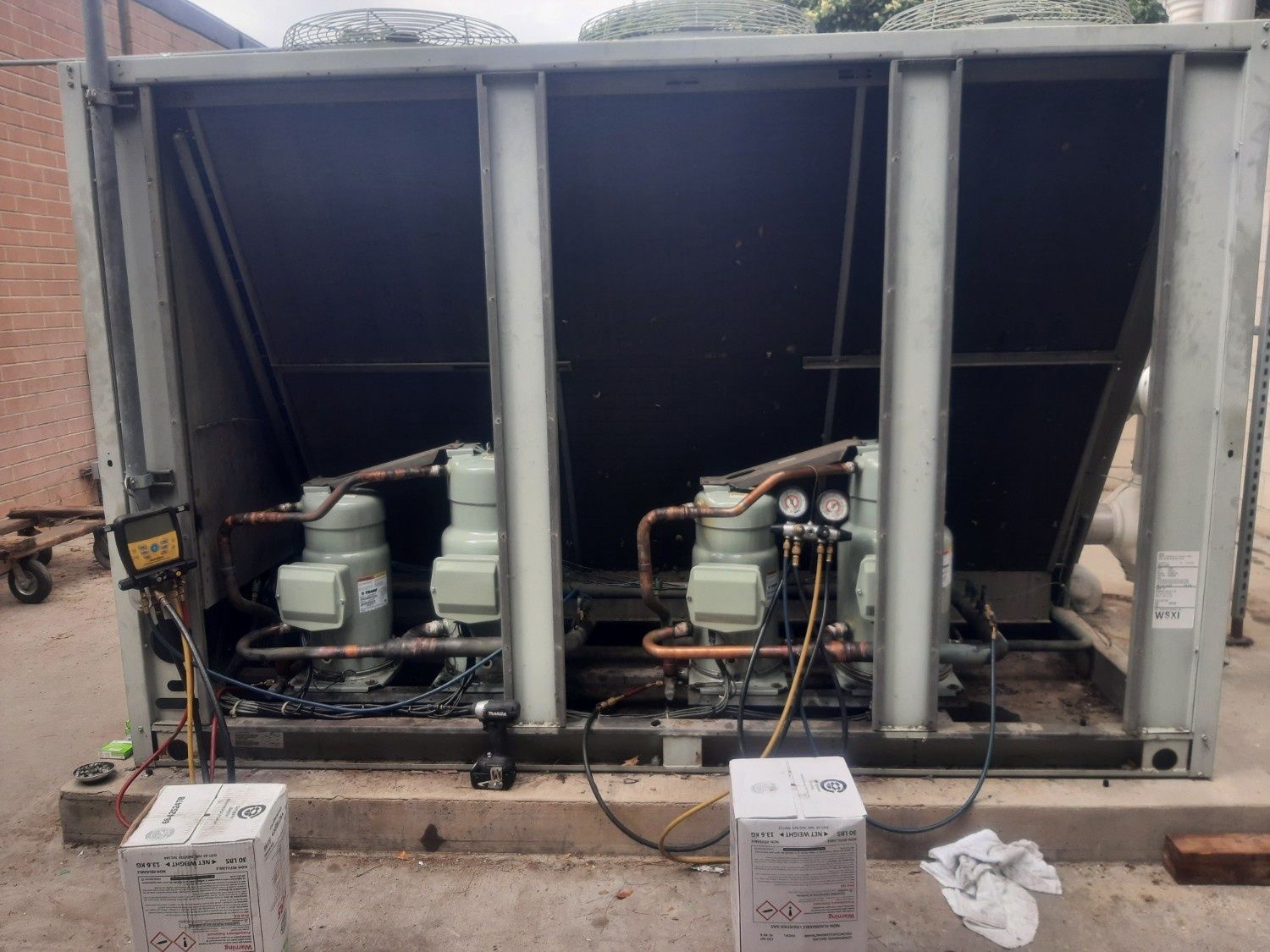 Two compressors inside a large industrial HVAC unit outdoors, with tools and equipment boxes nearby.