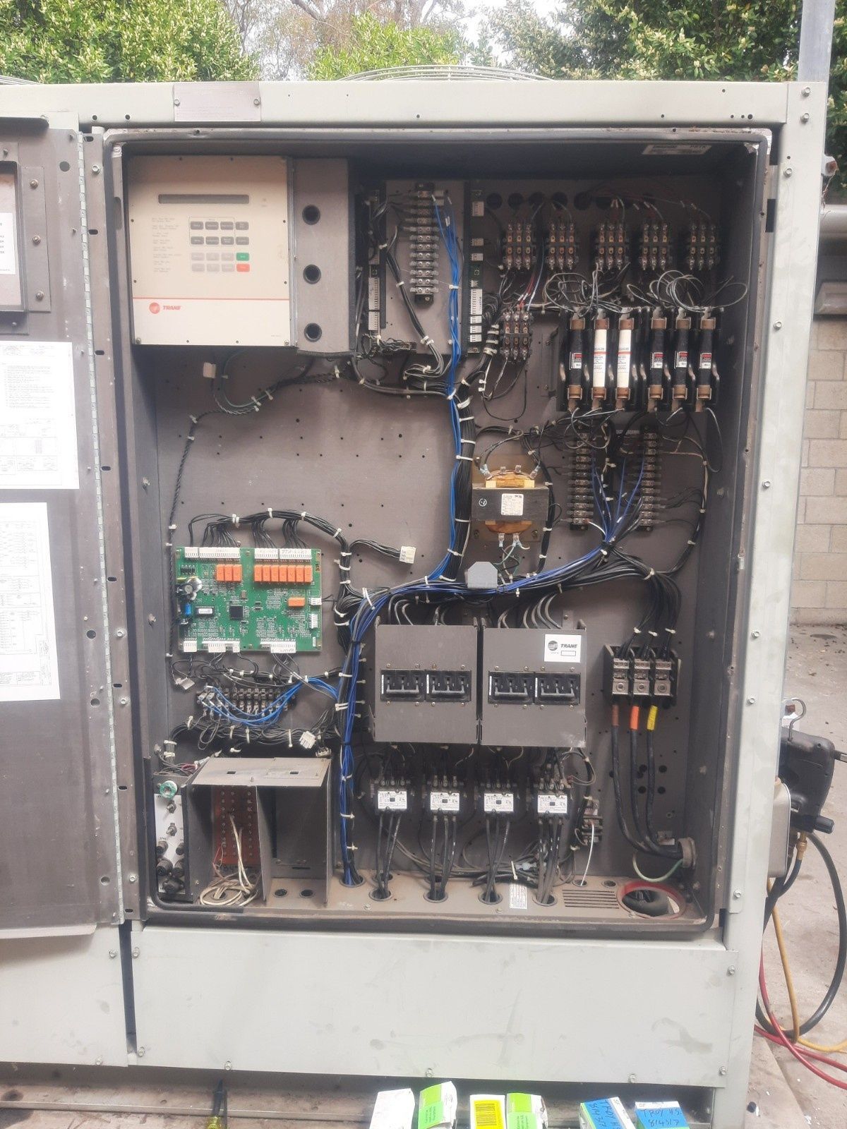 The open panel of an industrial electrical control box containing circuit boards, wires, fuses, and various relays.