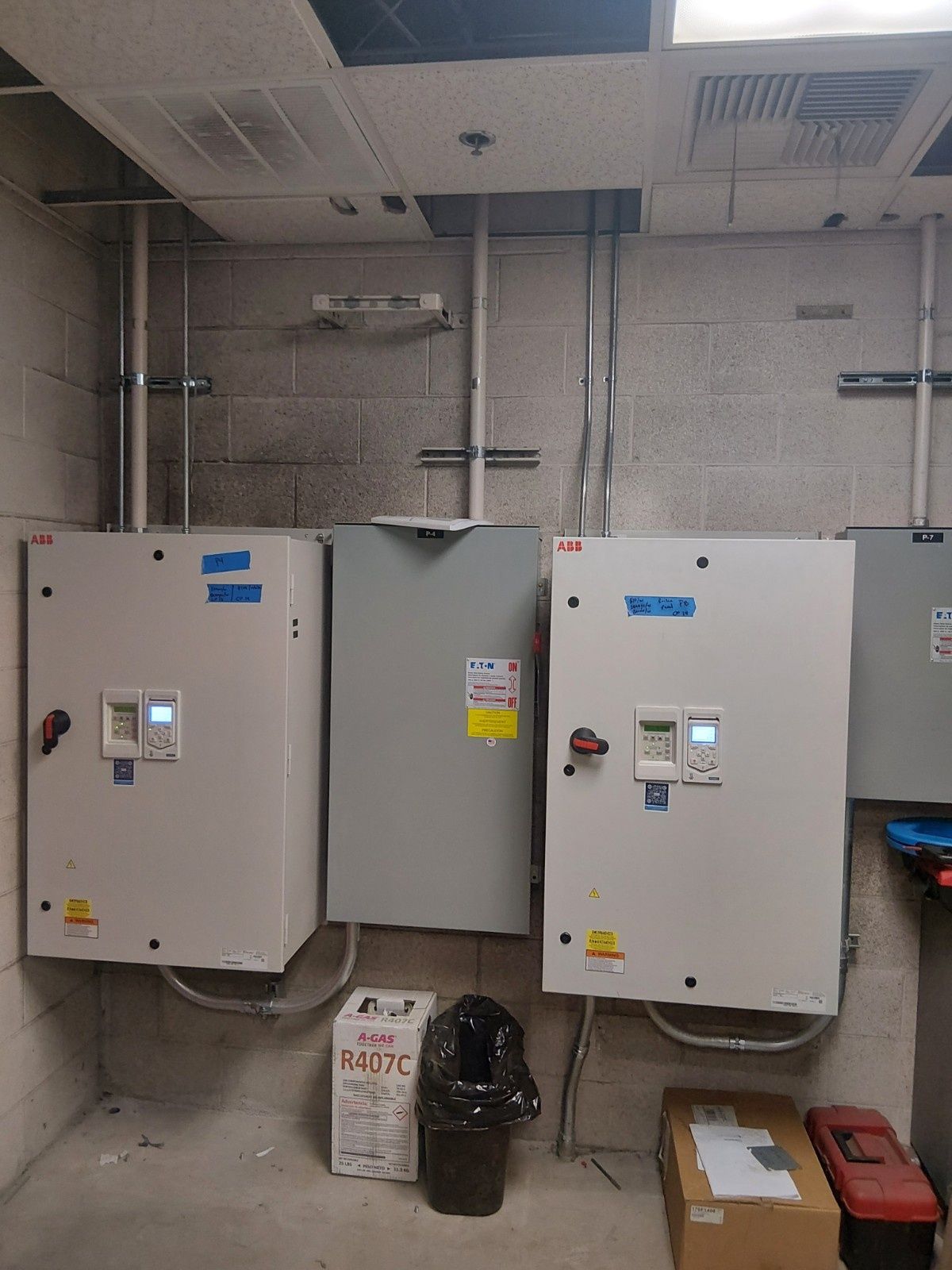 Two large white automatic transfer switches mounted on a gray cinderblock wall with electrical conduit above.