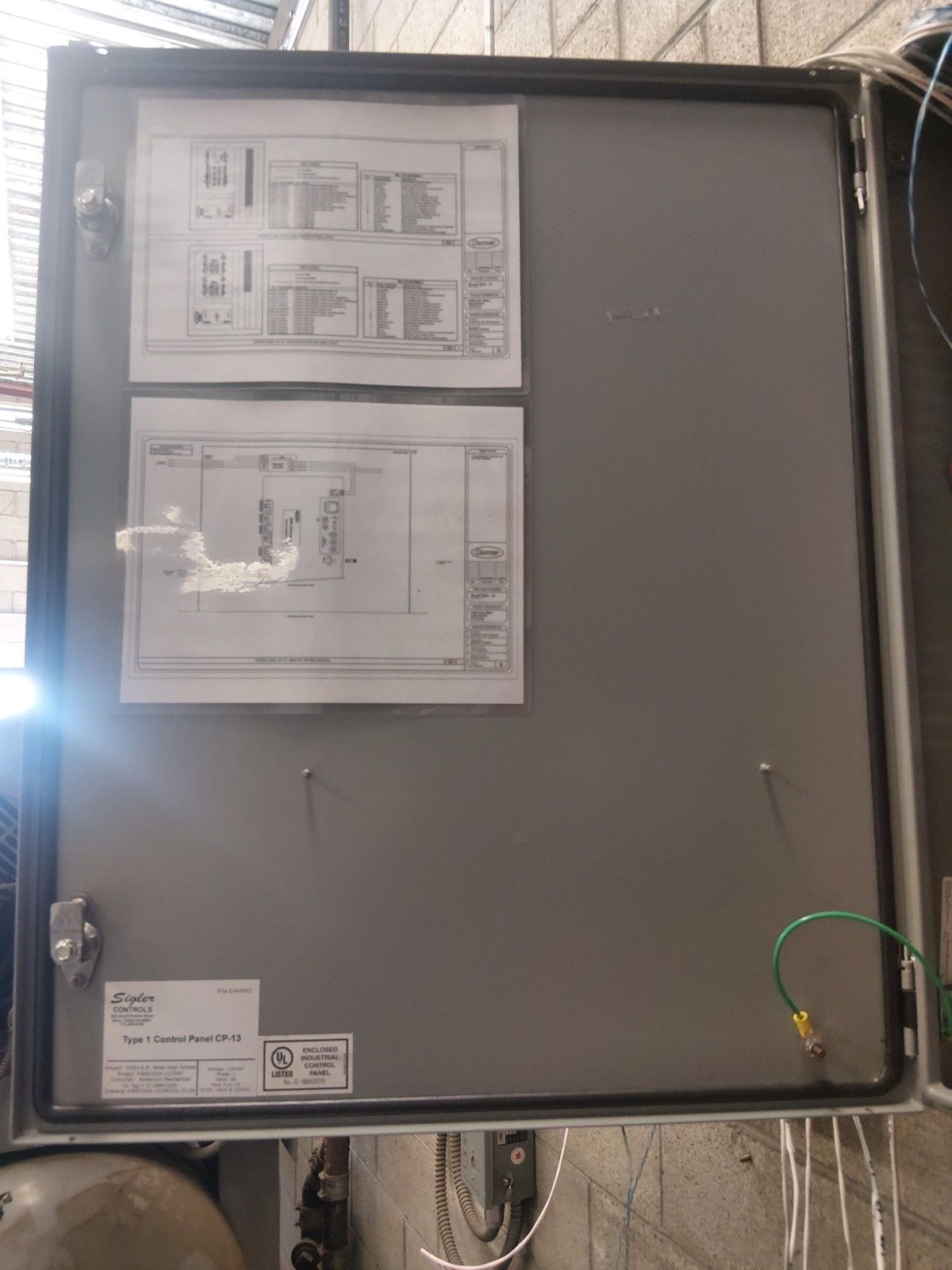 An open metal electrical enclosure mounted on a wall, featuring two wiring diagrams attached to its inner door panel.