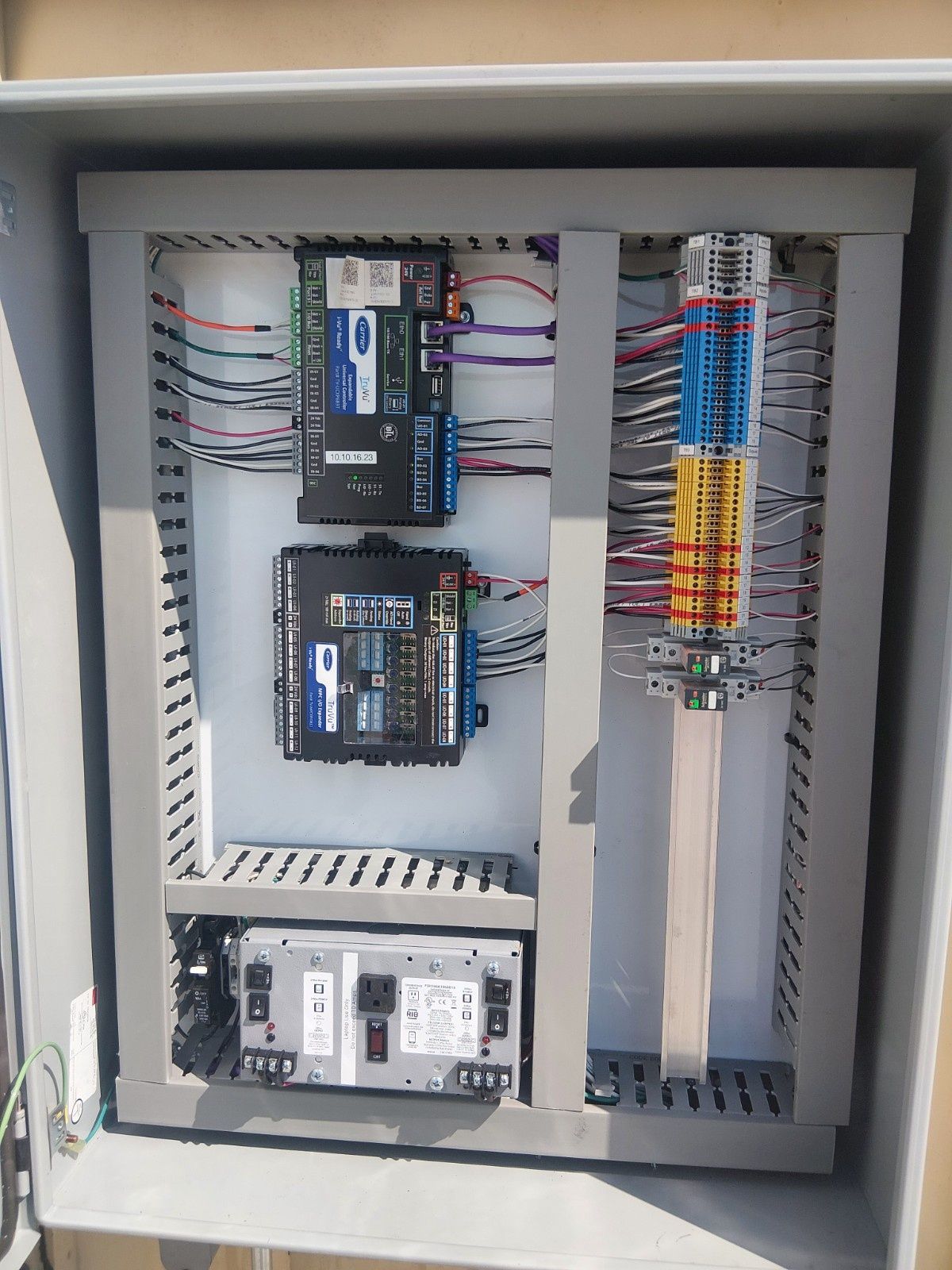 An electrical control panel enclosure mounted on a wall, showing interior wiring, circuit boards, and a power supply.