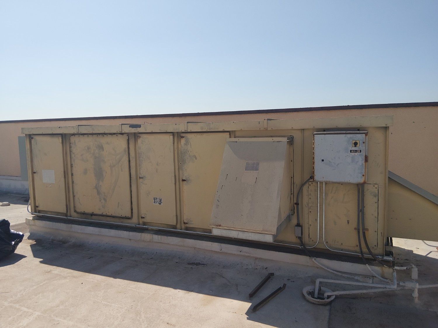 A beige rooftop HVAC unit with access panels and an attached electrical box against a clear blue sky.