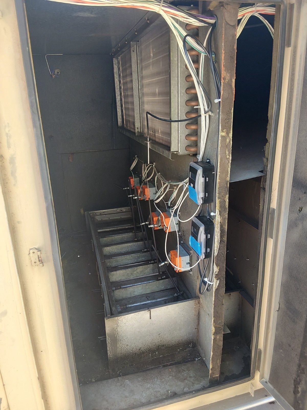 The interior of an industrial HVAC unit showing cooling coils, mechanical dampers, and control actuators.