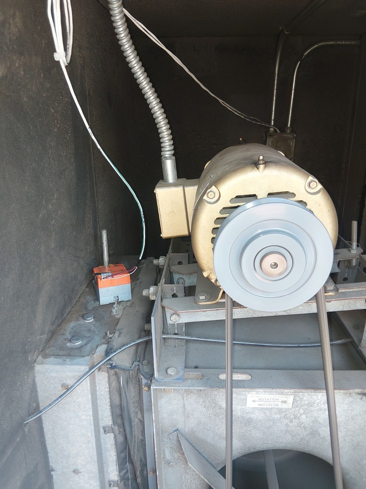 An electric motor with a belt drive mounted inside a dark, industrial equipment enclosure.