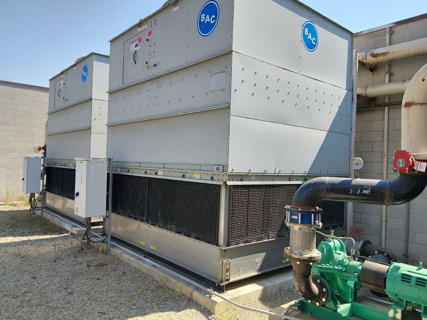 Two industrial BAC cooling towers installed outdoors on a gravel ground with a green water pump in the foreground.
