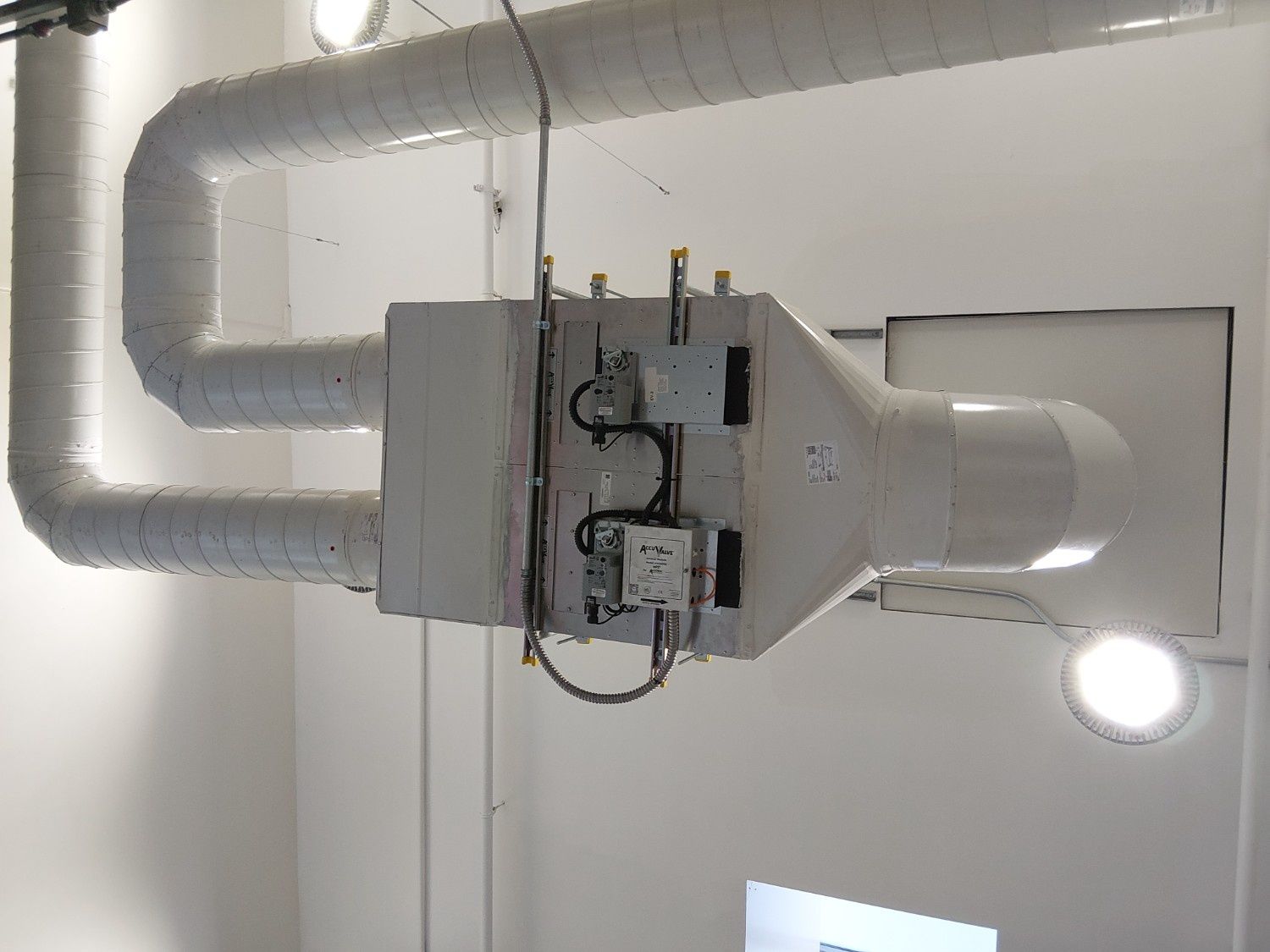 A white industrial HVAC unit suspended from a white ceiling, connected by insulated ductwork with electrical controls.
