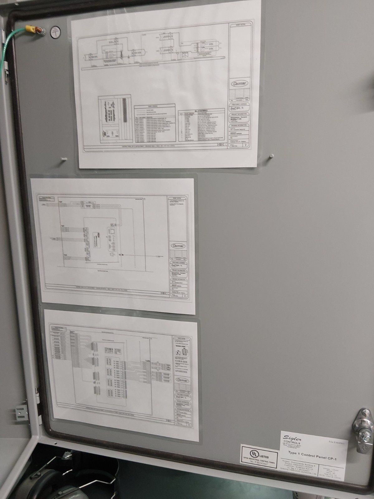 Three electrical schematic diagrams taped inside a metal industrial control cabinet door.