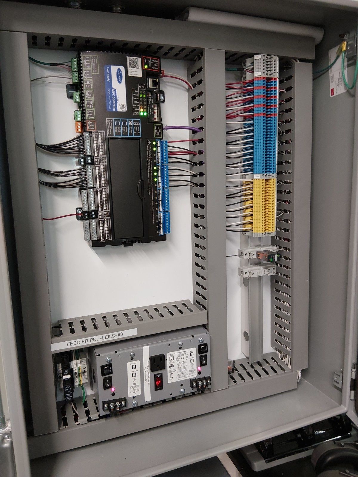 An open electrical control panel with a controller, power supply, and terminal blocks mounted inside a gray enclosure.