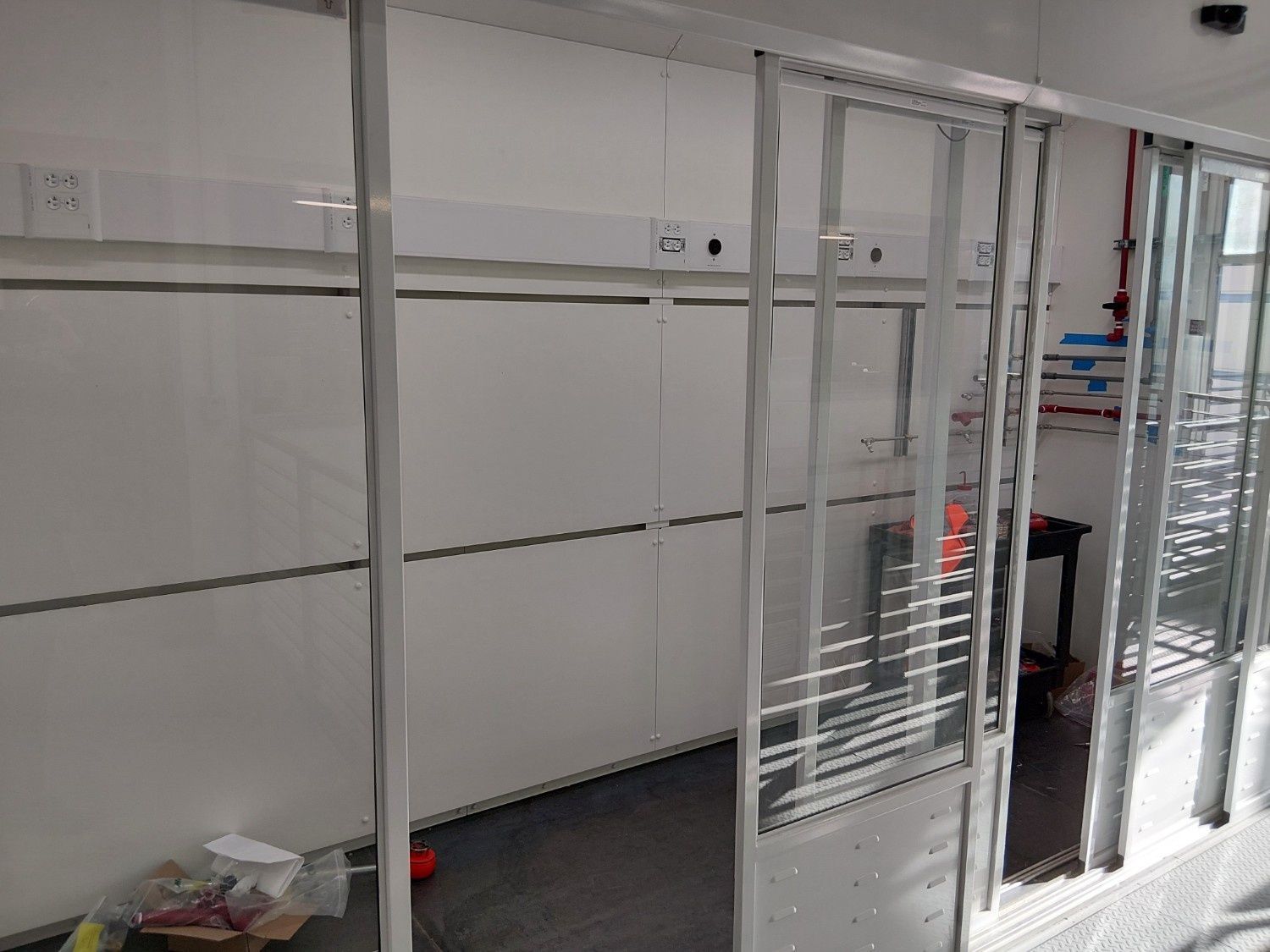 An interior view of a room under construction, featuring white wall panels, a metal frame partition, and electrical outlets.