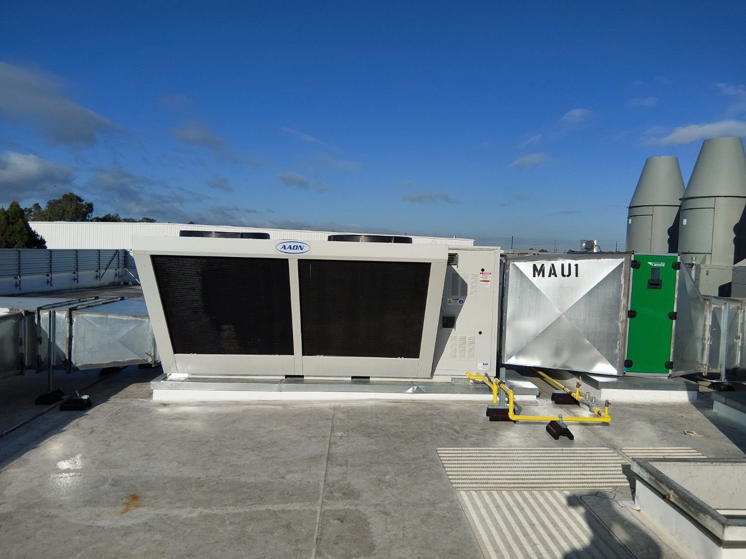 Large commercial HVAC unit with fans and a metal duct system situated on a flat rooftop against a clear blue sky.