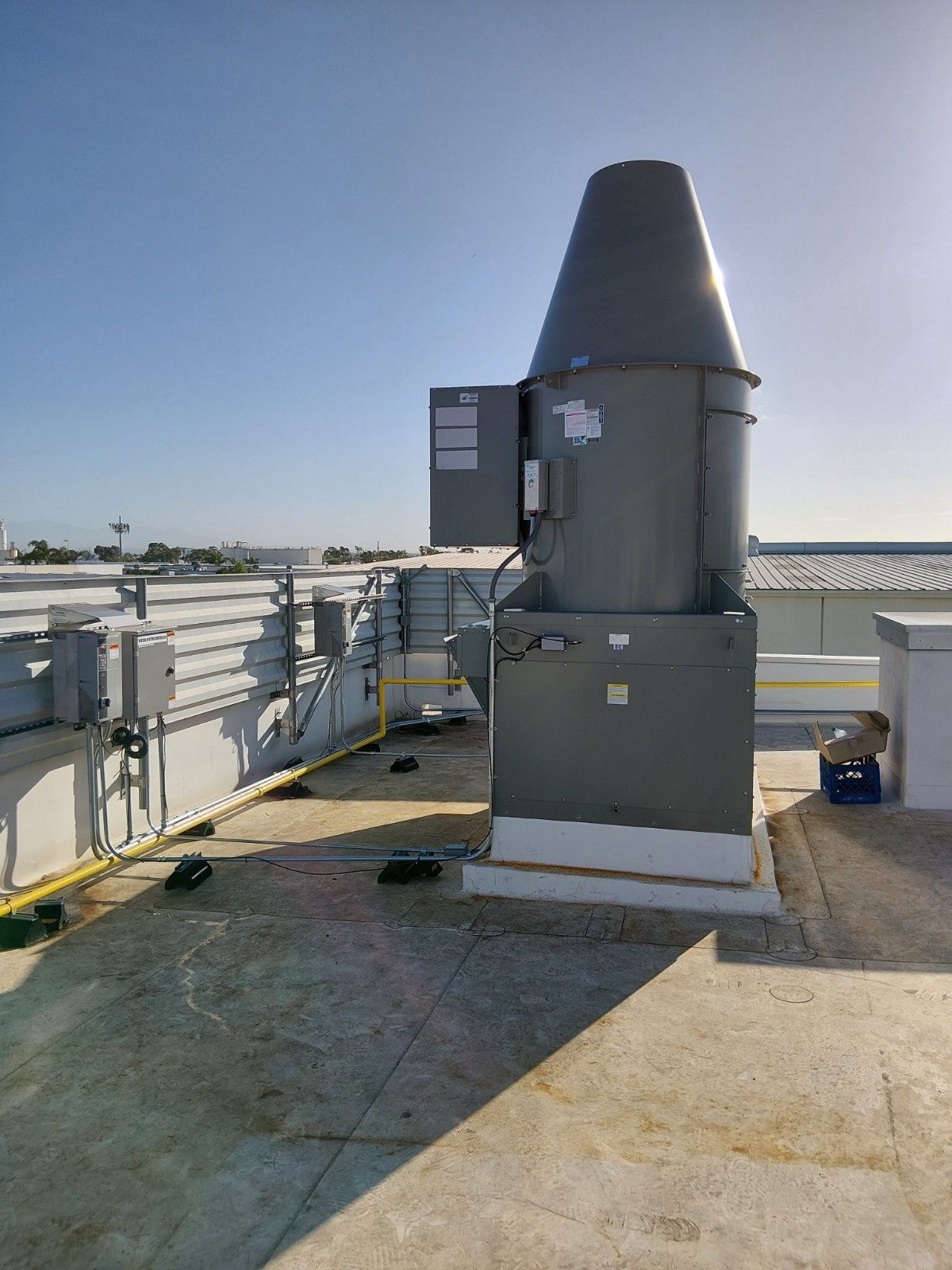 A gray industrial exhaust fan mounted on a flat rooftop against a clear blue sky.