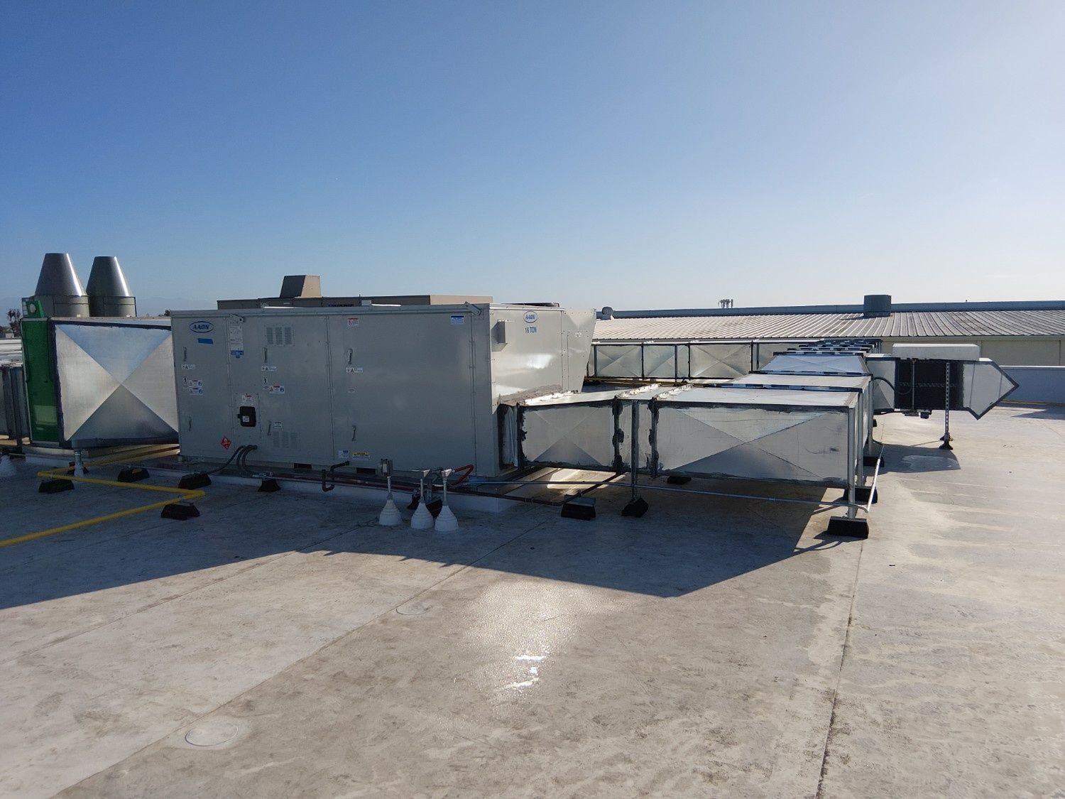 A commercial rooftop HVAC unit with silver metal ductwork under a clear blue sky.