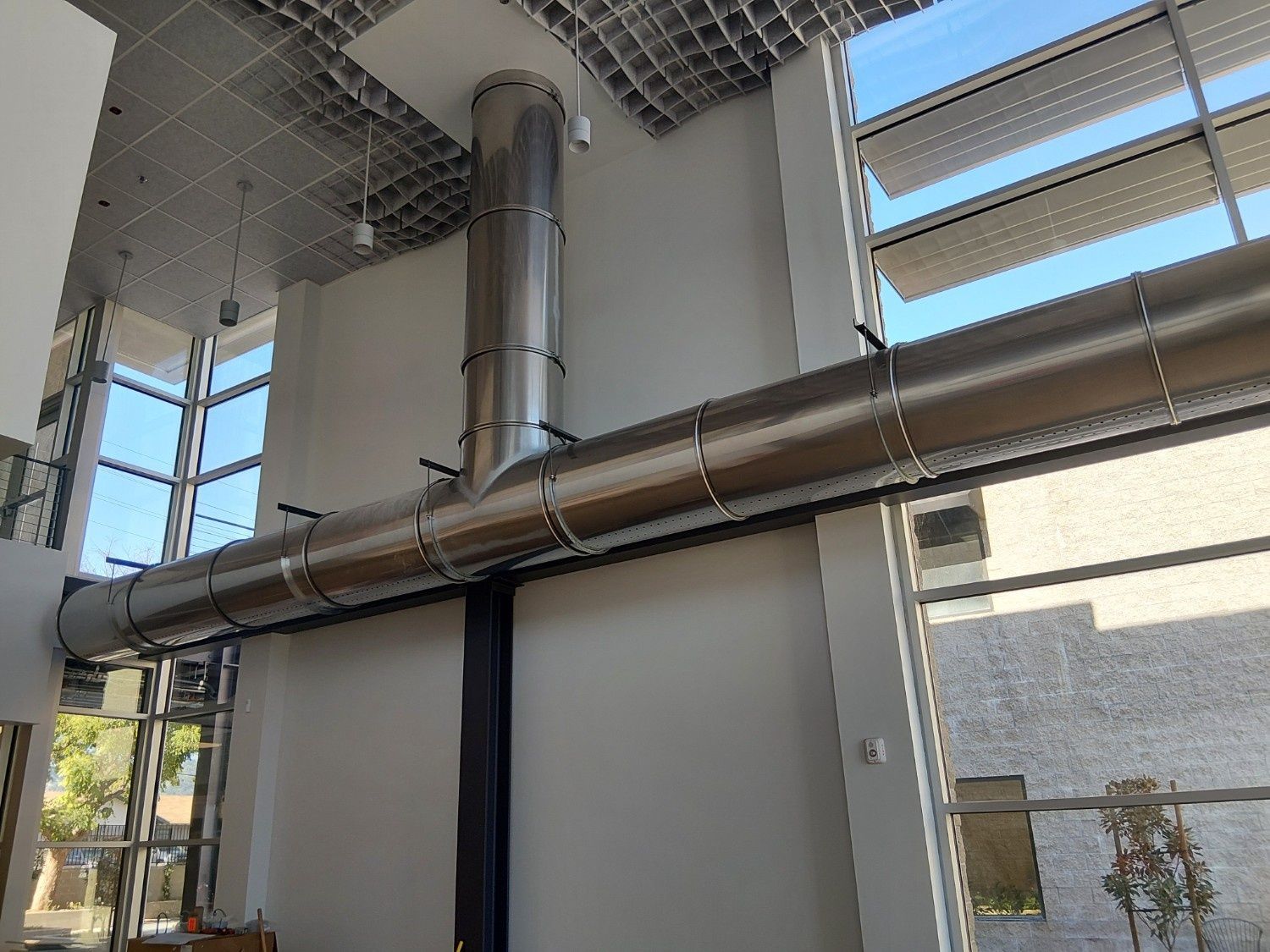 Large, cylindrical metal ventilation ducts installed in a modern, high-ceilinged room with glass windows.