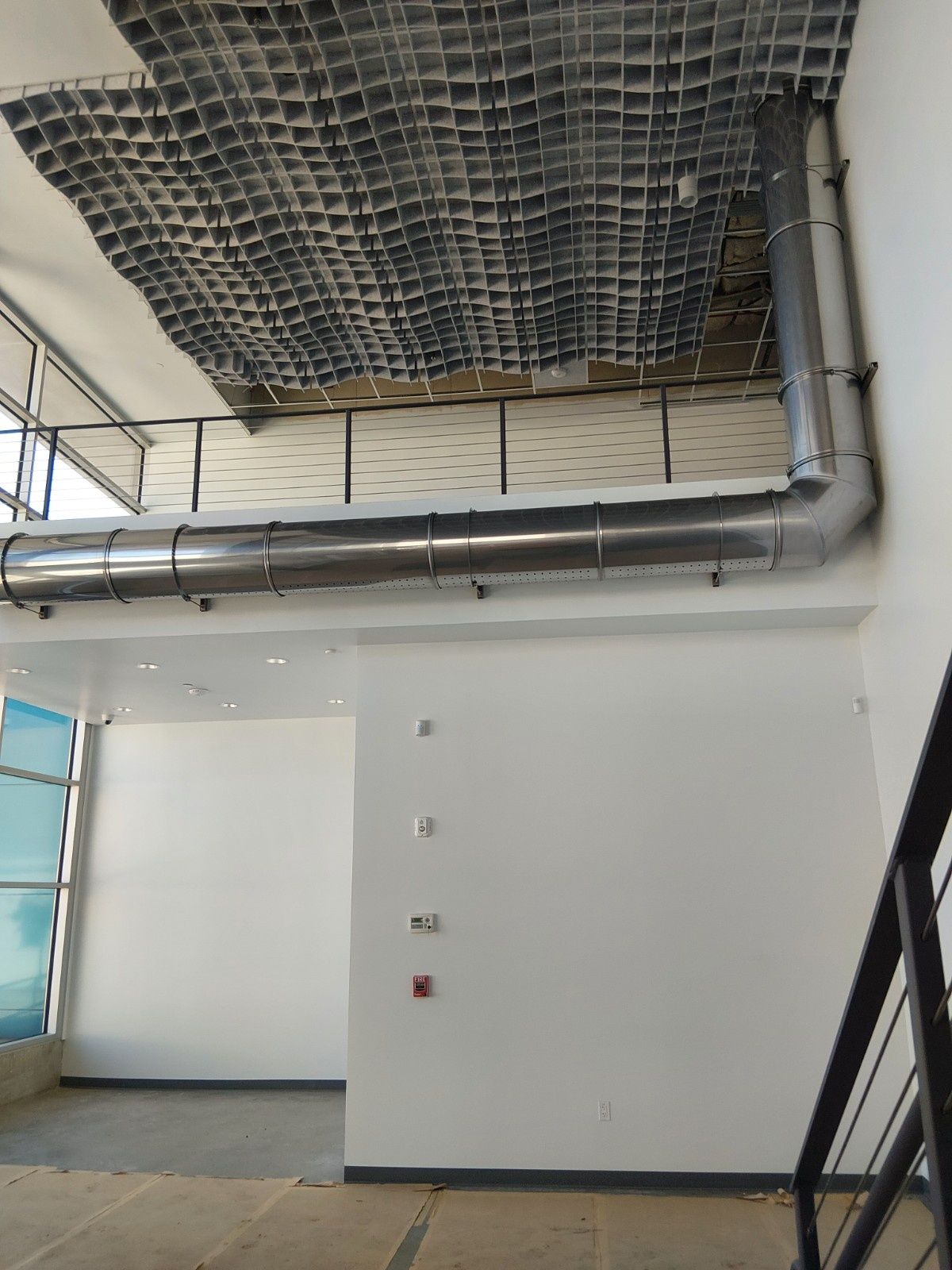 An interior view of a room under construction with a metal duct running along the wall and an exposed grid ceiling.