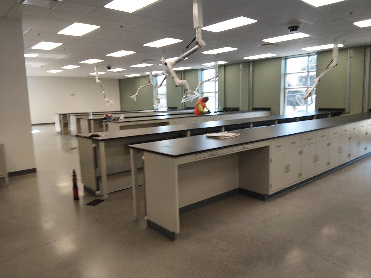 A wide view of a modern, empty science laboratory featuring multiple long rows of lab benches and ceiling-mounted arms.