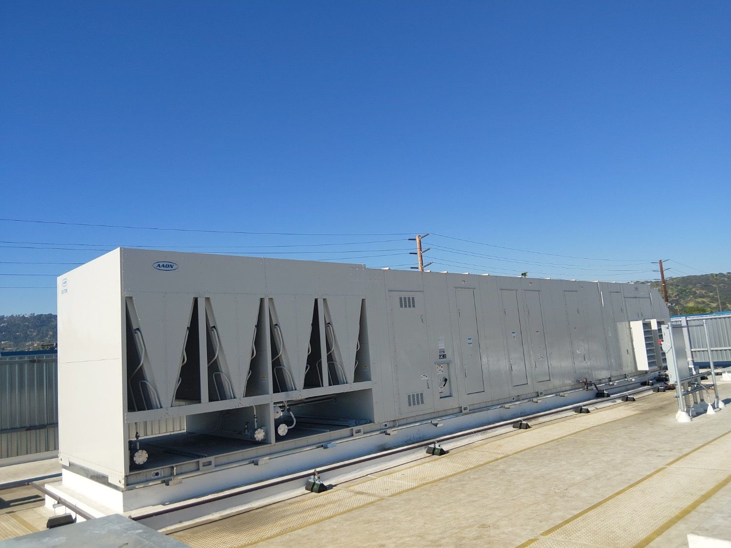 Large, beige industrial chiller unit with V-shaped cooling coils, situated on a flat rooftop against a clear blue sky.