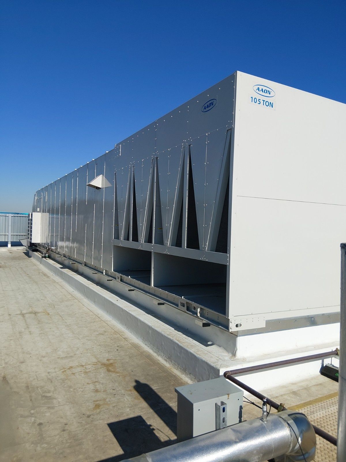 A large, rectangular HVAC industrial cooling unit sits on a flat building rooftop under a clear blue sky.