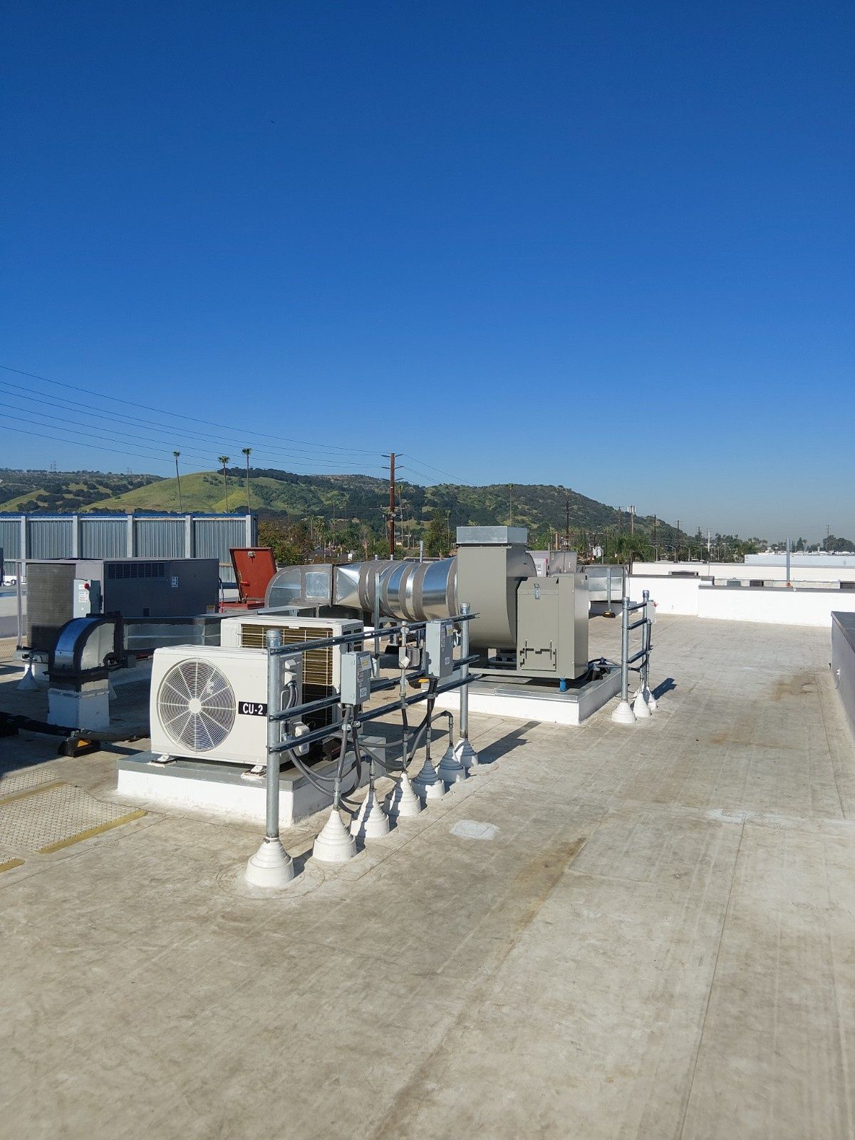 Commercial HVAC units mounted on a flat, white gravel roof under a clear blue sky, with a mountain in the background.
