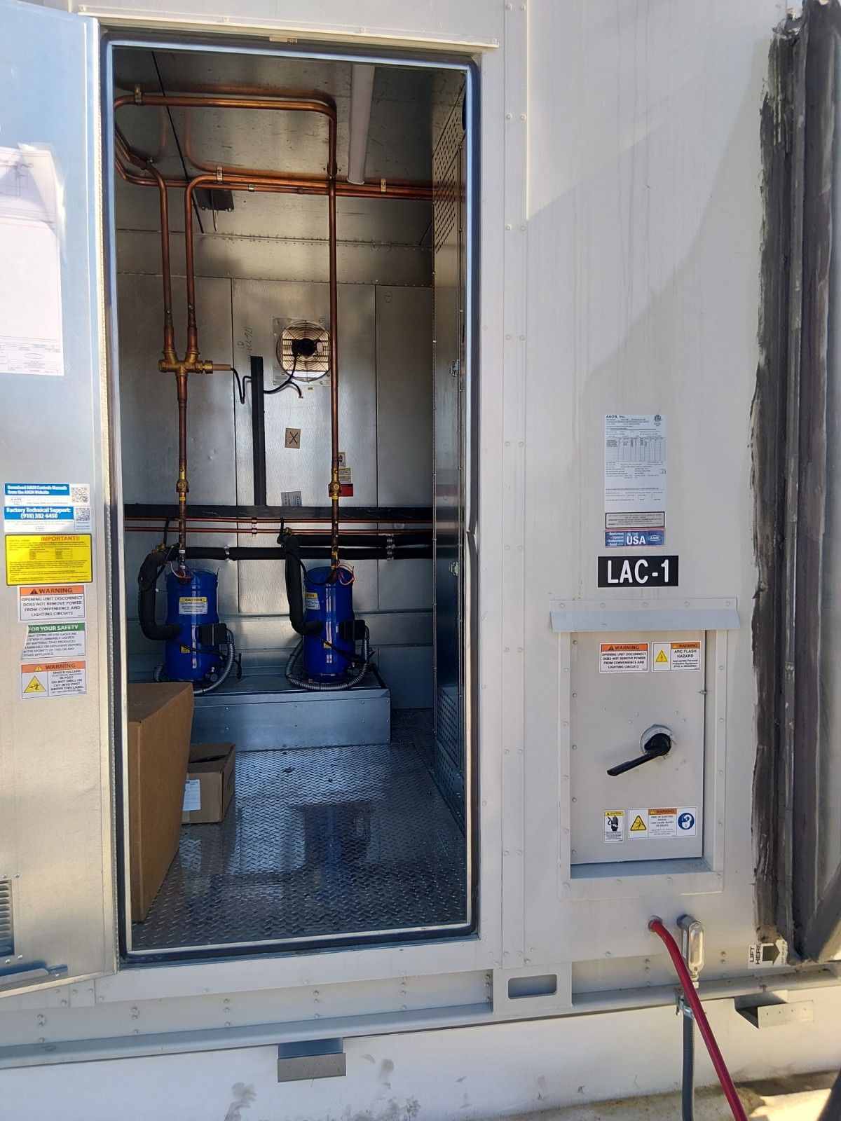 A utility cabinet with its door open, revealing two blue water pumps inside connected by copper piping.