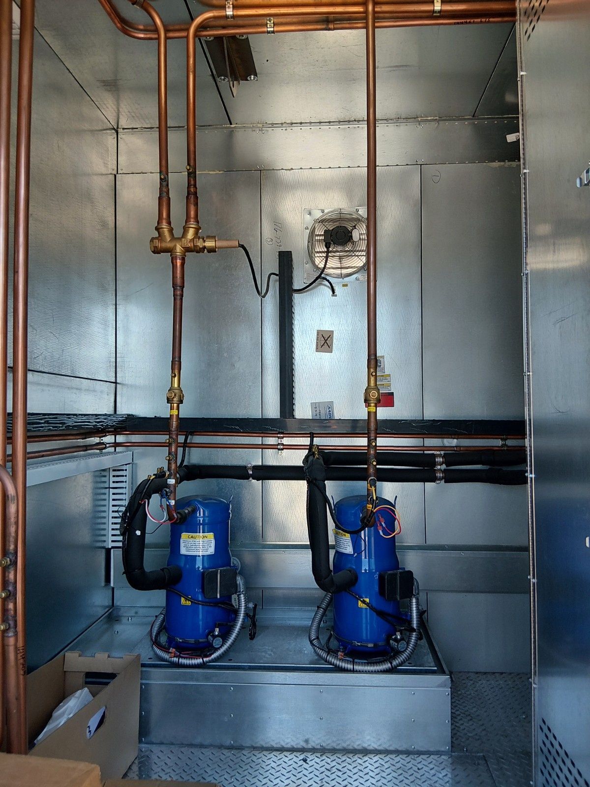 Two blue industrial refrigeration compressors installed in a metallic enclosure with copper piping connected to the tops.