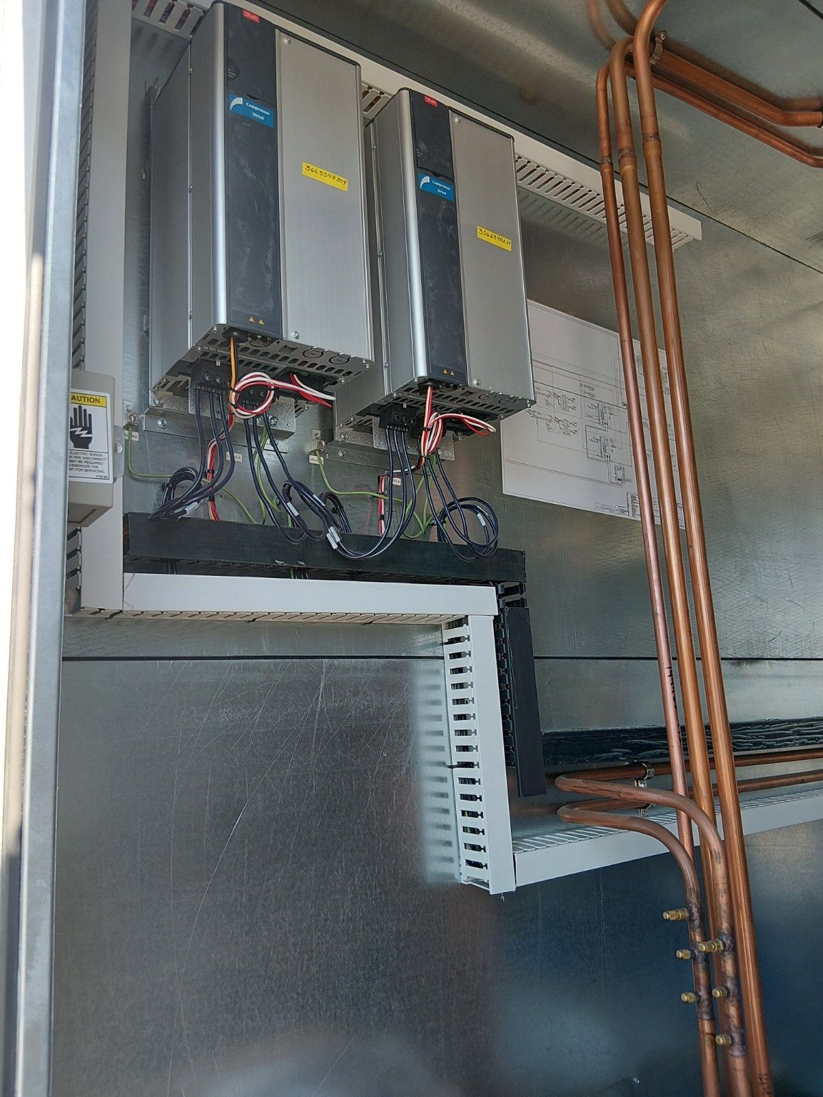 Two metal industrial control units mounted inside a metal enclosure with vertical copper pipes on the right.