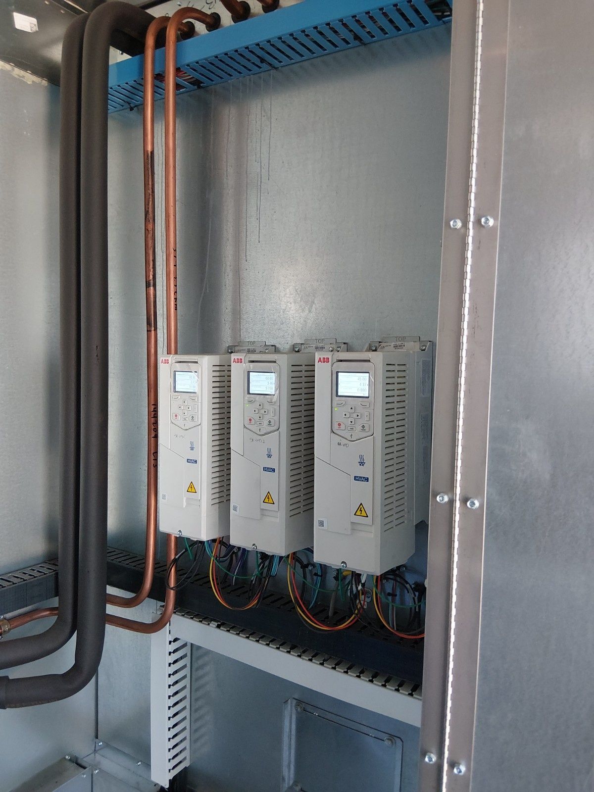 Three ABB industrial variable frequency drives mounted on a metal wall inside a panel with copper piping.