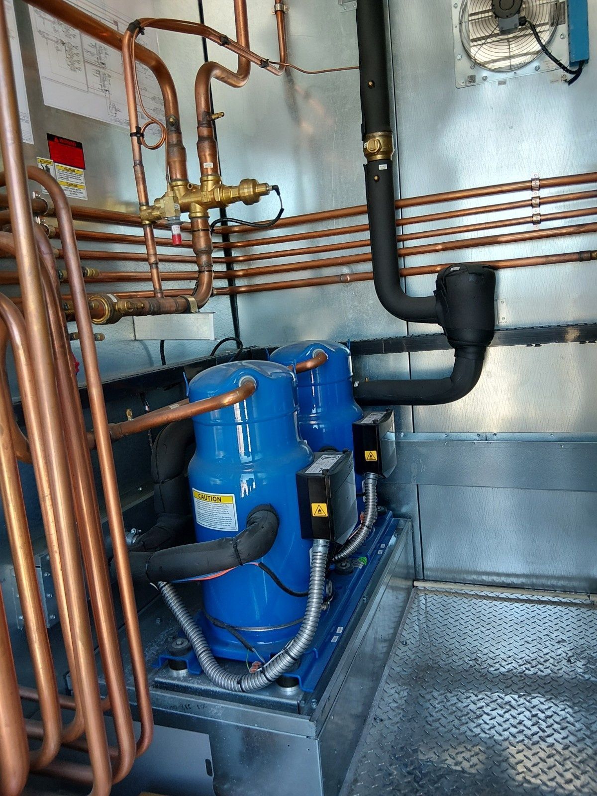 Two blue industrial compressors inside a metal mechanical enclosure with copper piping.