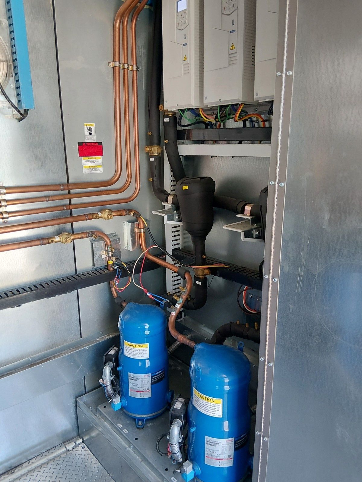 An industrial HVAC compressor cabinet containing two blue compressors, copper refrigerant piping, and electrical controls.
