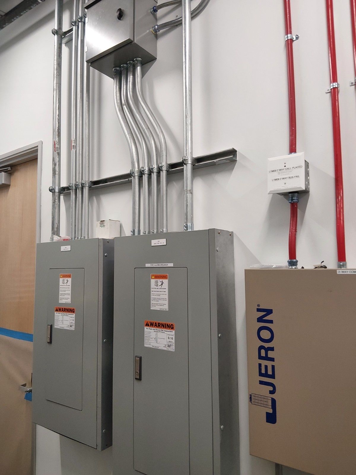 Electrical panels and wiring conduits mounted on a white wall, including a Jeron communication control unit.