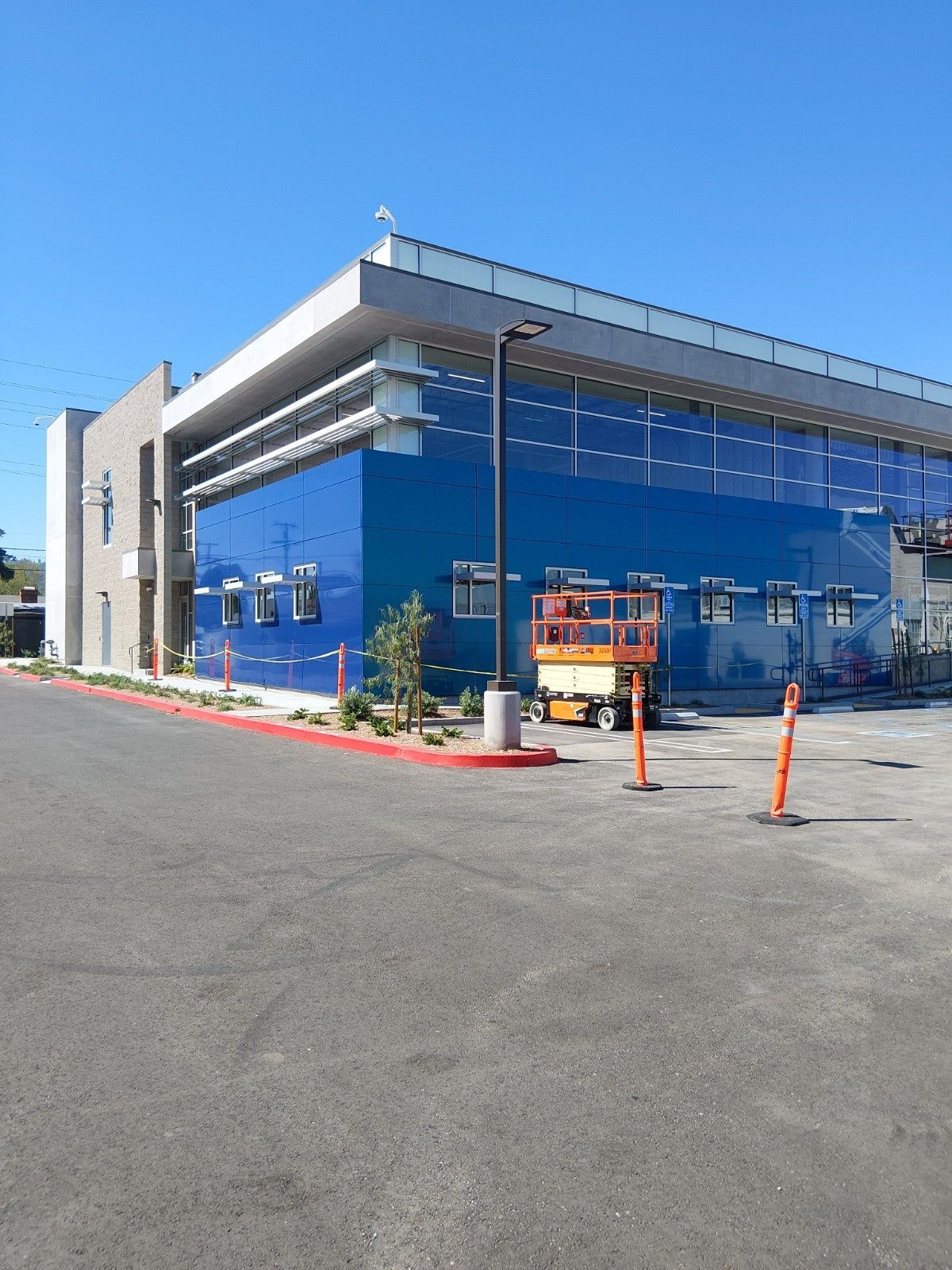 Modern building with a blue facade, a grey concrete section, and a construction lift parked on the asphalt lot.