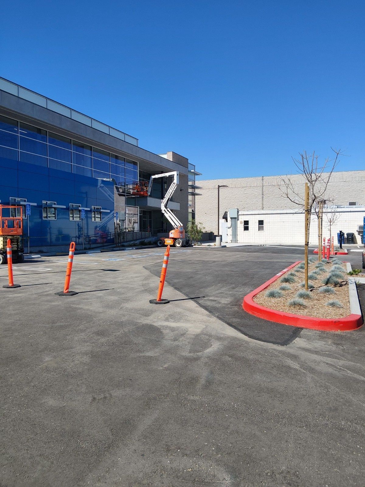 A building with a blue glass exterior and an articulating boom lift, with construction cones in a paved parking lot.