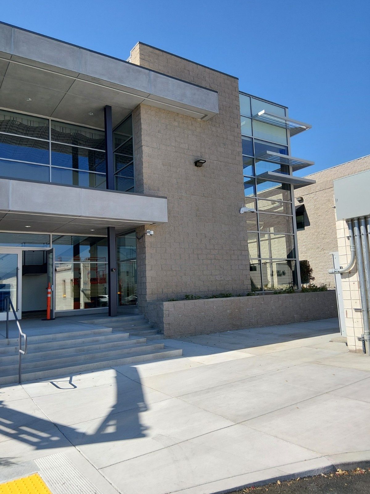 A modern building entrance with stairs and a ramp, featuring stone-textured walls and glass windows under a clear sky.