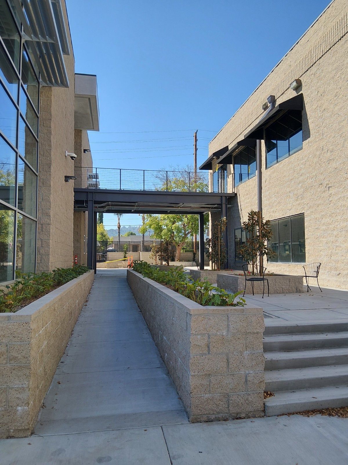 A stone pathway between two buildings features a ramp on the left, a staircase on the right, and a metal bridge overhead.