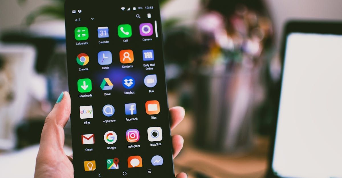 A hand holding a smartphone showing an app drawer interface with various colorful icons on a black background.