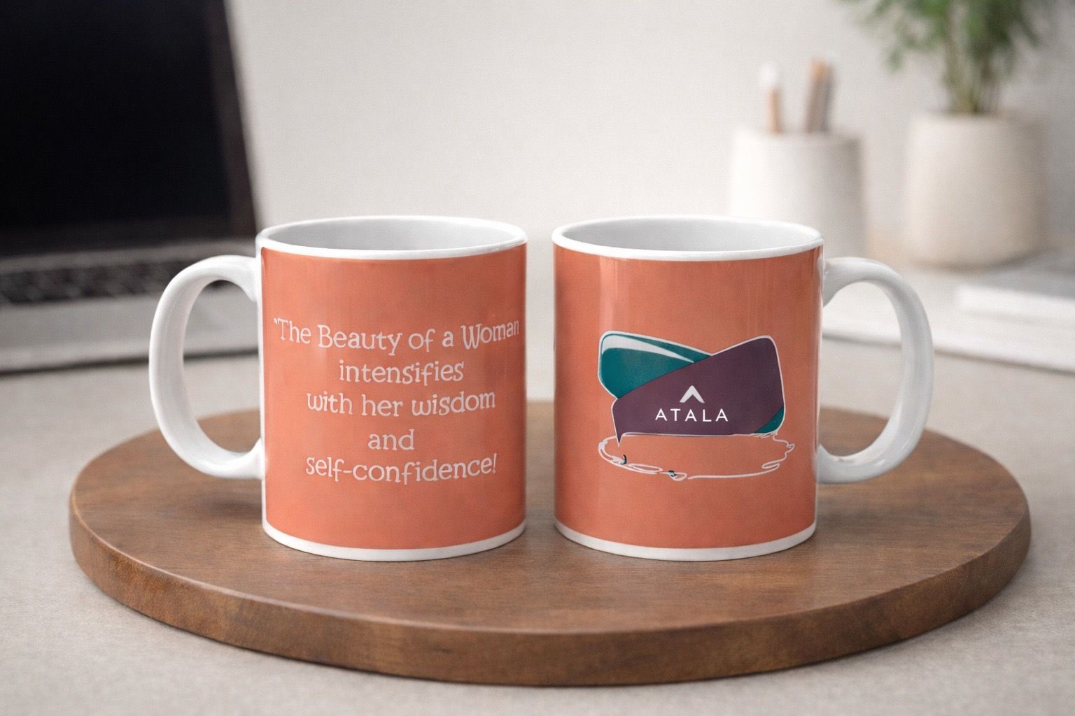 Two orange mugs on a wooden tray; one displays an inspirational quote, the other features an Atala logo.