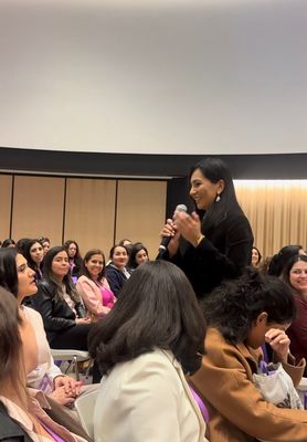 Speaker at a podium in a conference room, addressing an audience with a laptop and microphone nearby.