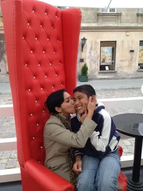 Woman kissing a boy's cheek while sitting in a large red chair outdoors.