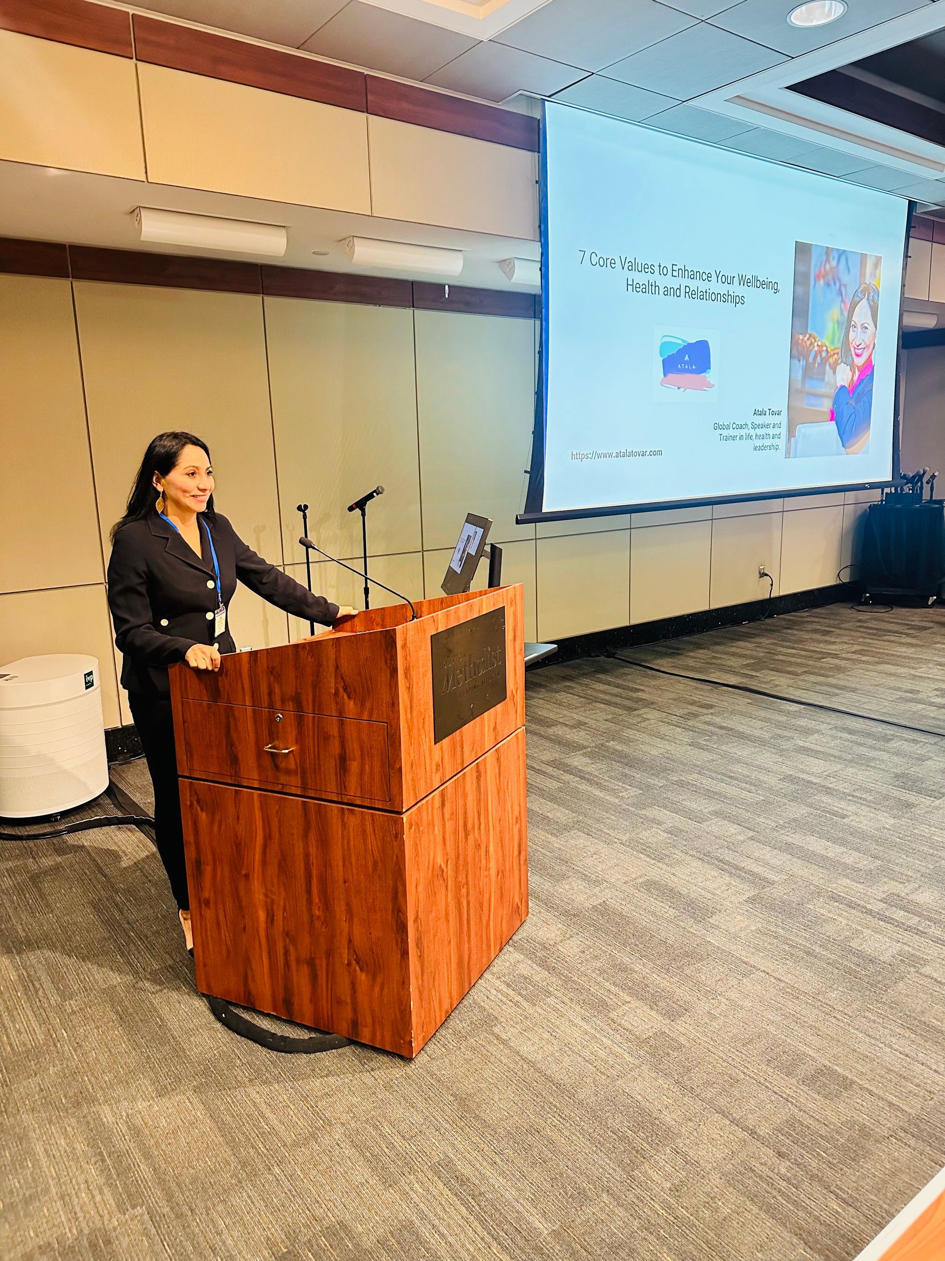 Woman presenting at a podium, large screen behind her. 