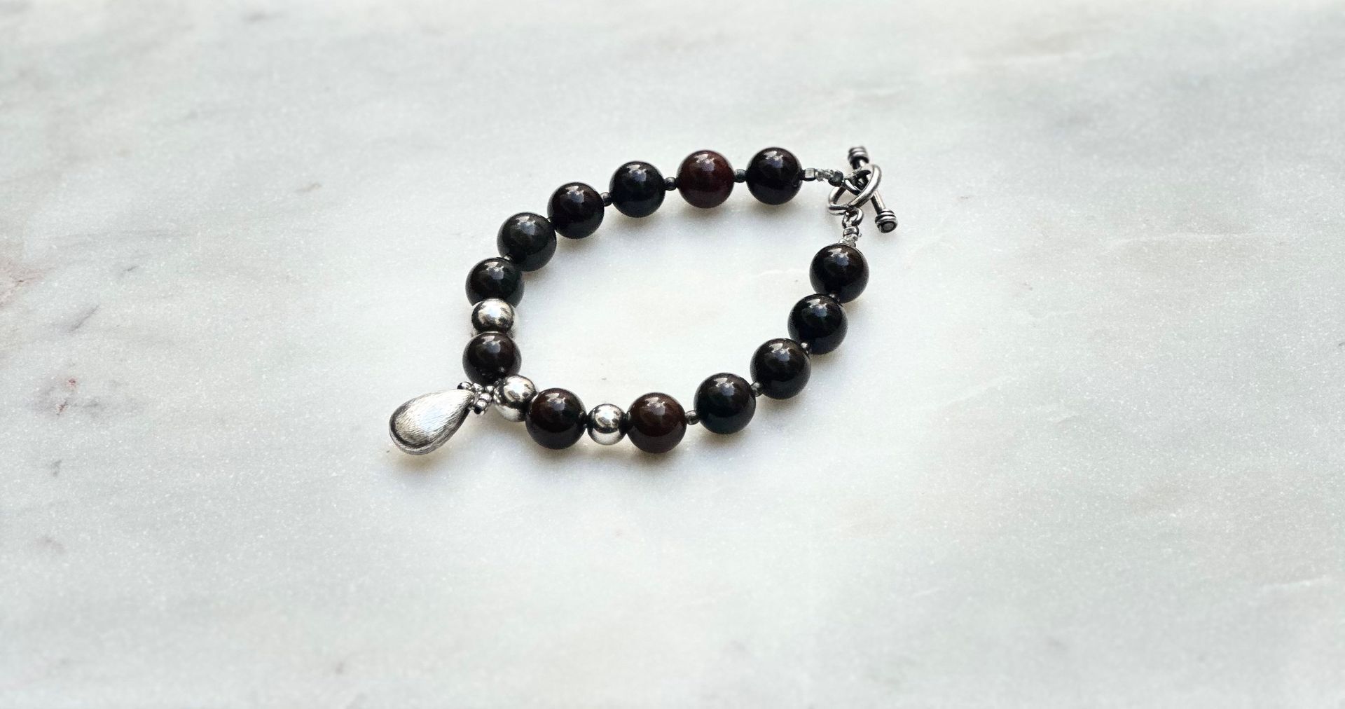 Dark beaded bracelet with silver clasp on white marble surface.