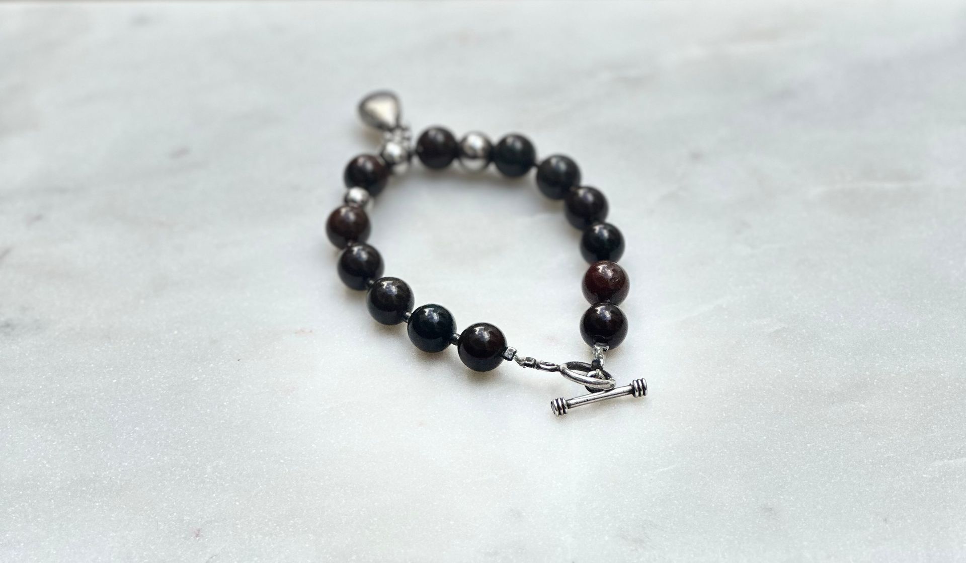 Dark beaded bracelet with silver clasp on white marble surface.