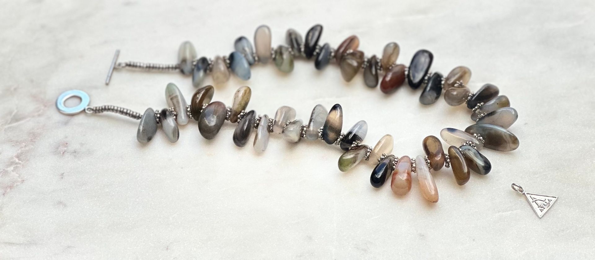 Bracelet made of gray and brown stones with a small triangular charm.