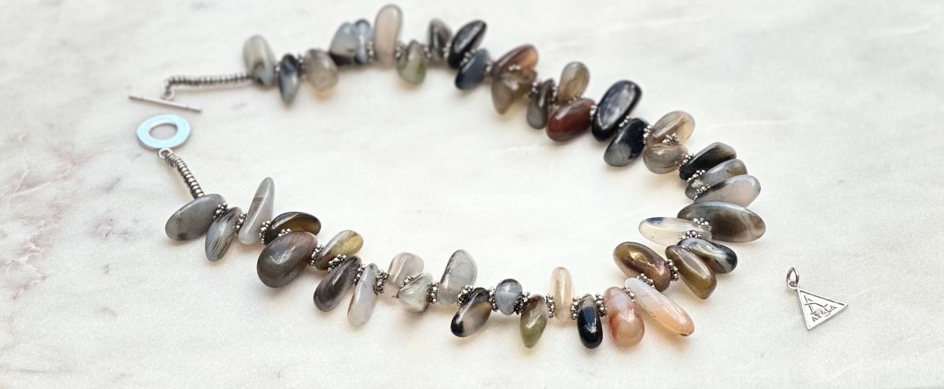 Bracelet made of gray and brown stones with a small triangular charm.