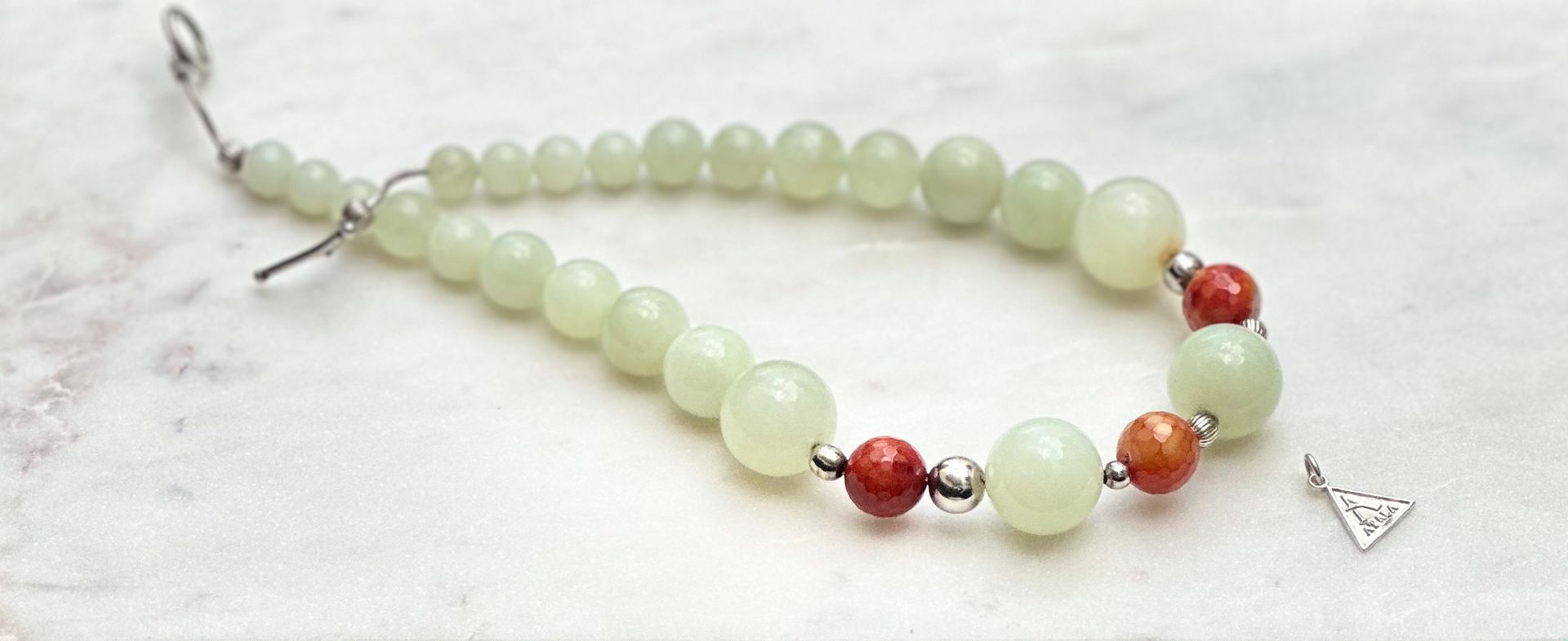 Beaded bracelet with pale green and red beads on a white surface with small pendant.