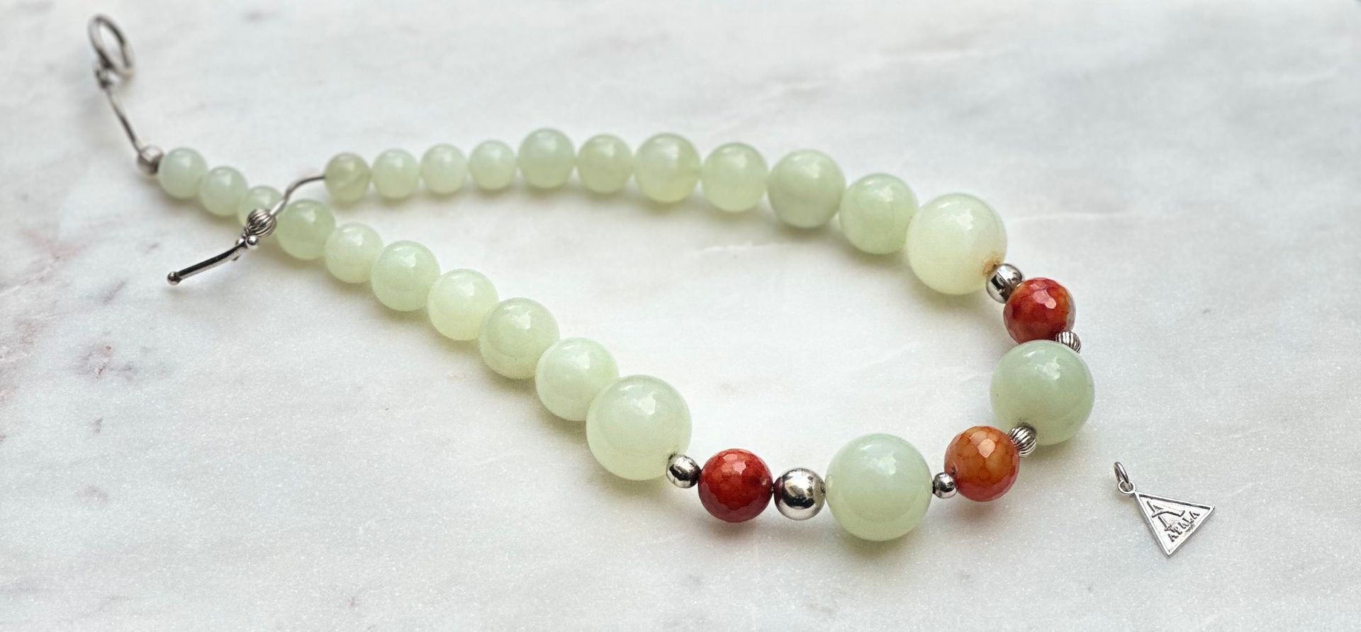 Beaded bracelet with pale green and red beads on a white surface with small pendant.