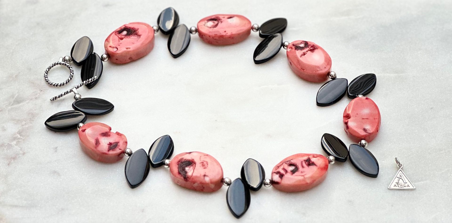 Necklace with pink and black stones on a white surface. Toggle clasp and pendant detail visible.